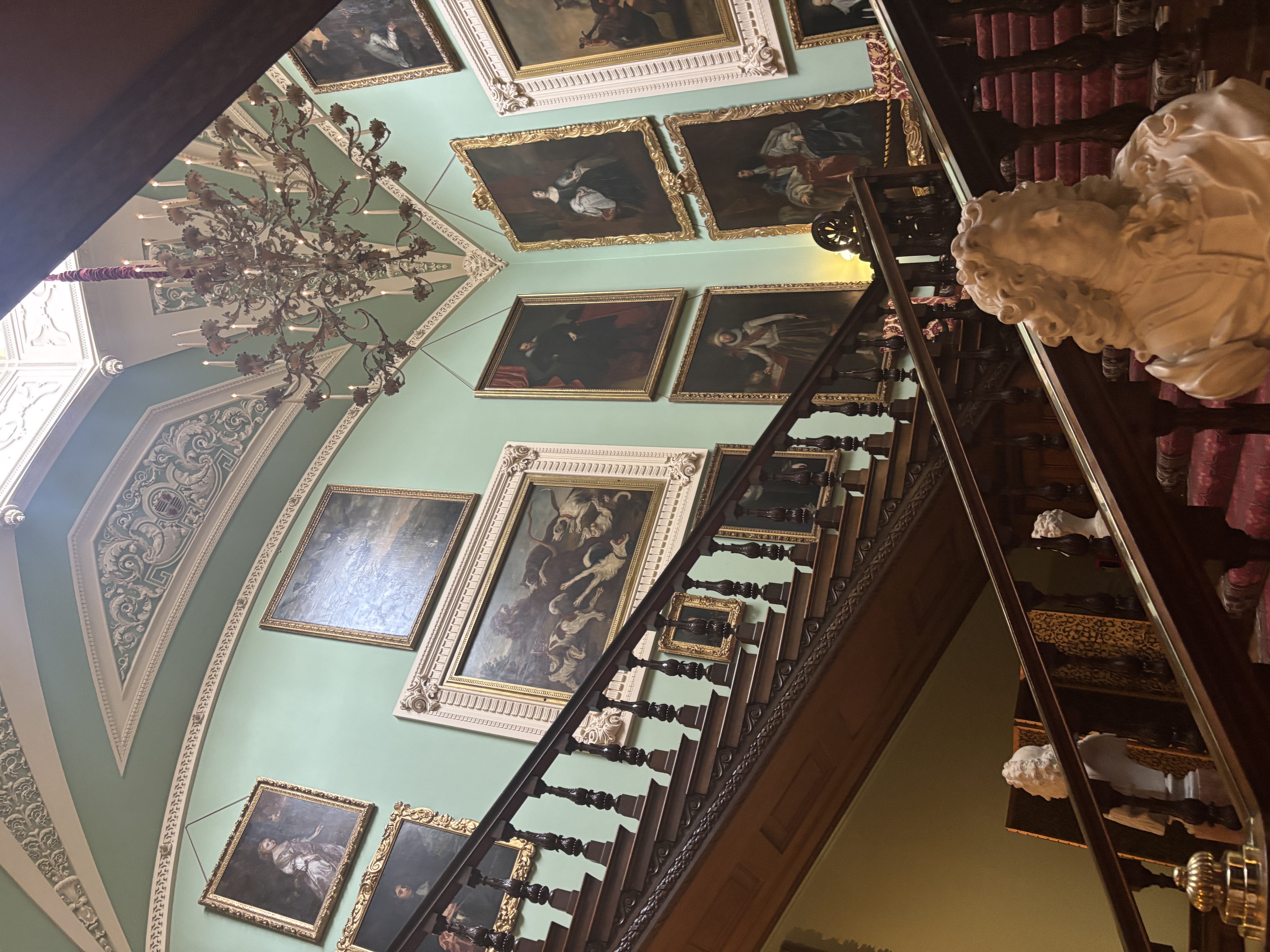 Interior shot of the grand staircase at Longleat, flanked by marble statues with paintings up the staircase